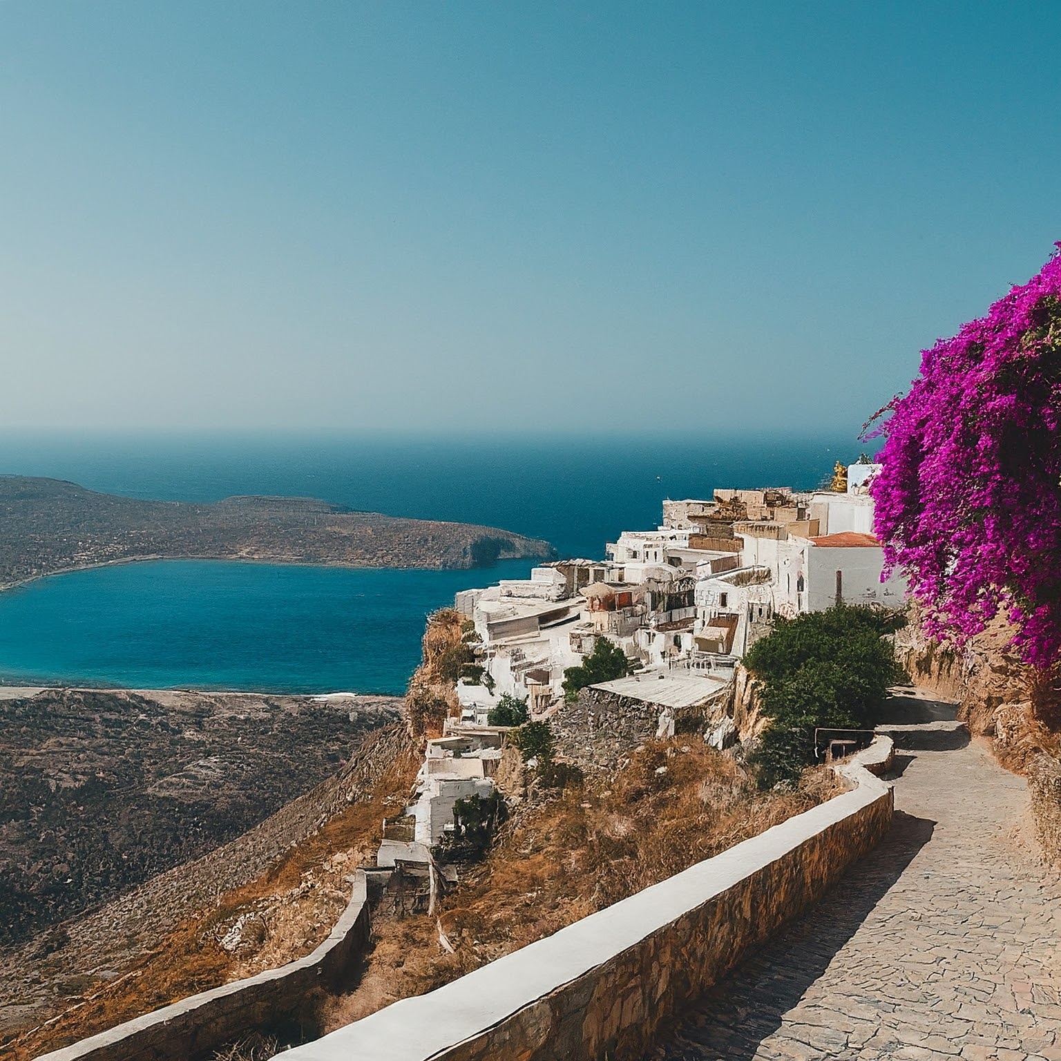 Traditional village in Crete, Greece, with whitewashed houses, bougainvillea flowers, and Aegean Sea view.