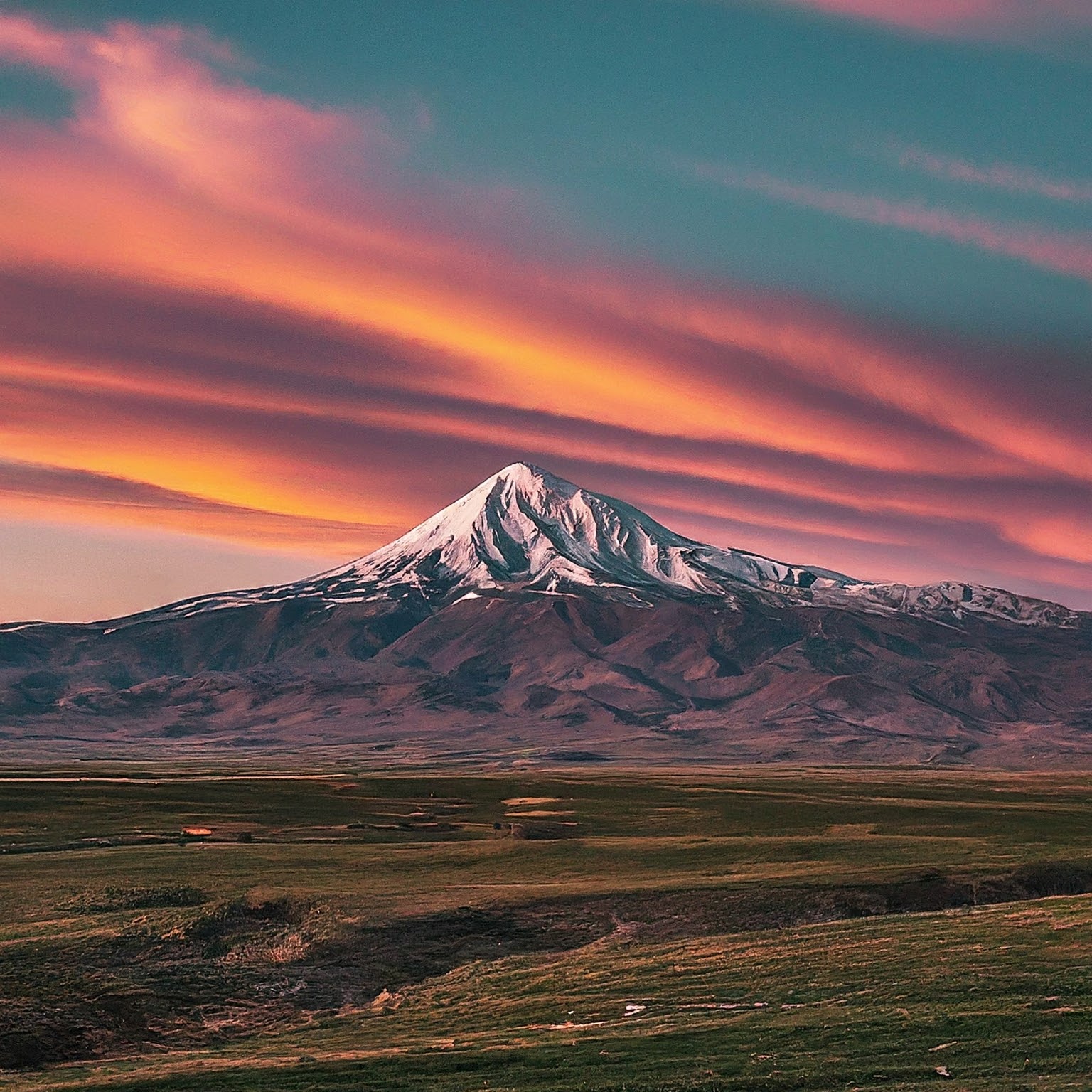 Sunrise over Mount Damavand, Iran, with golden light and colorful clouds.