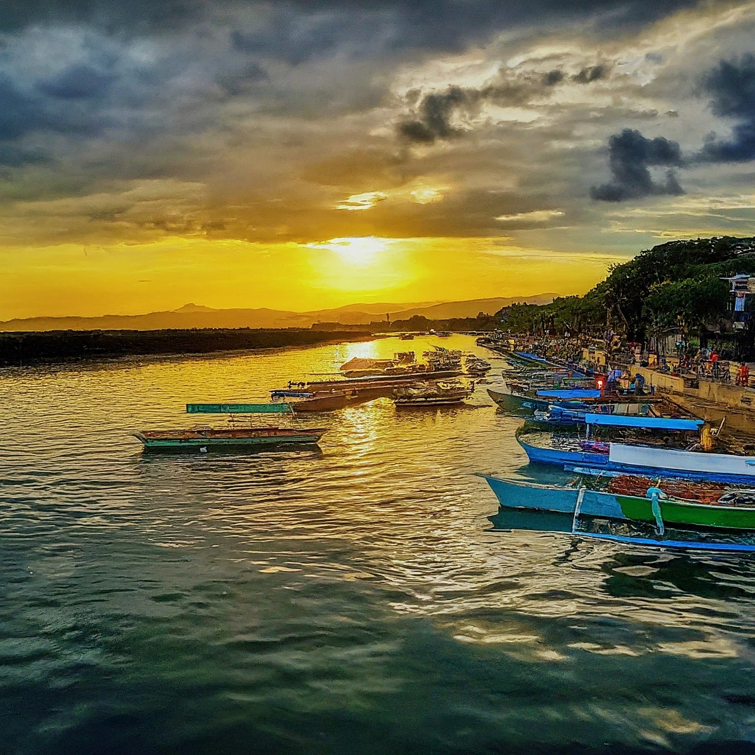 Sunset over Iloilo River Esplanade, Iloilo City, with colorful pump boats and people enjoying the waterfront.