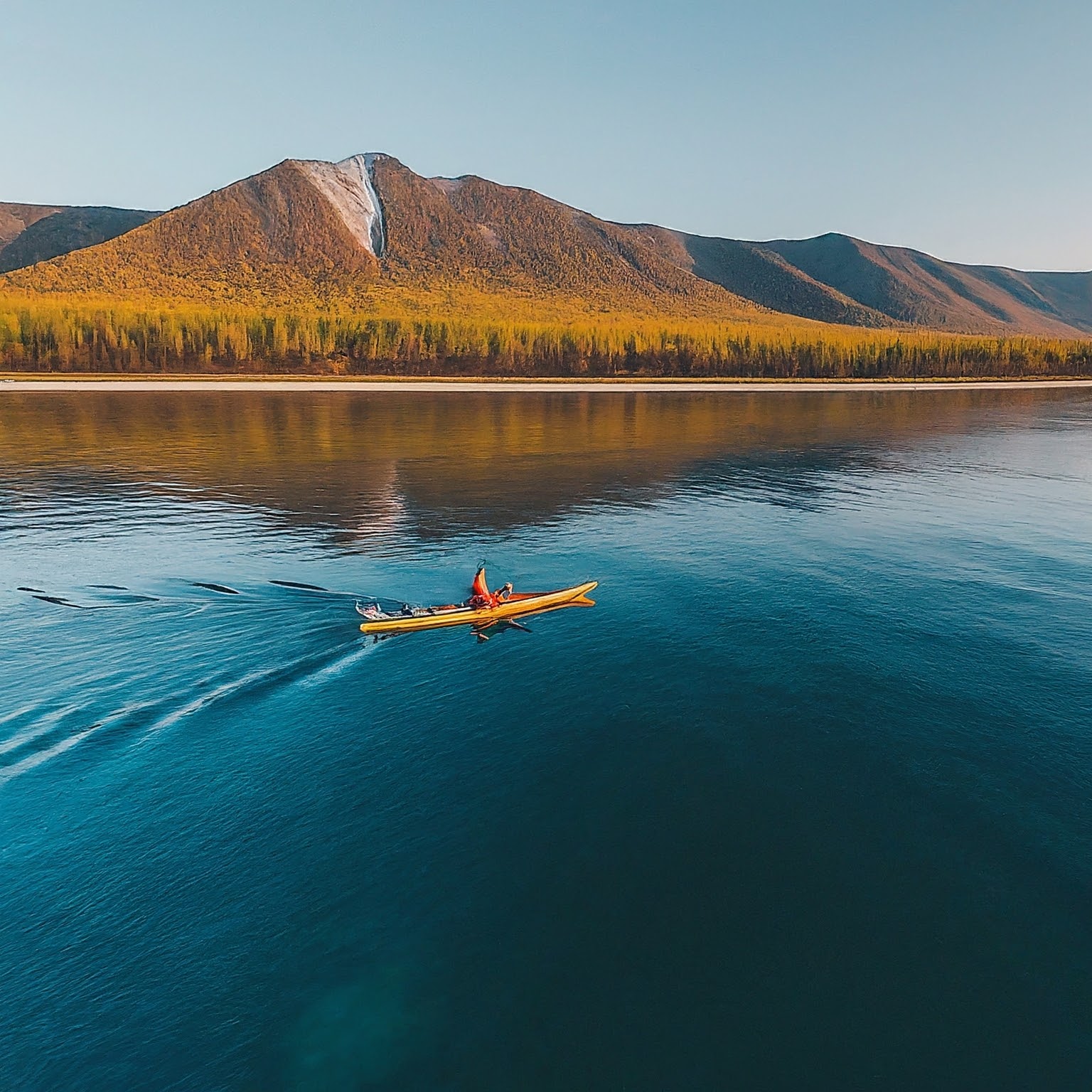 Kayaker exploring the clear waters of Lake Baikal, Russia, with mountains and forests in the background.