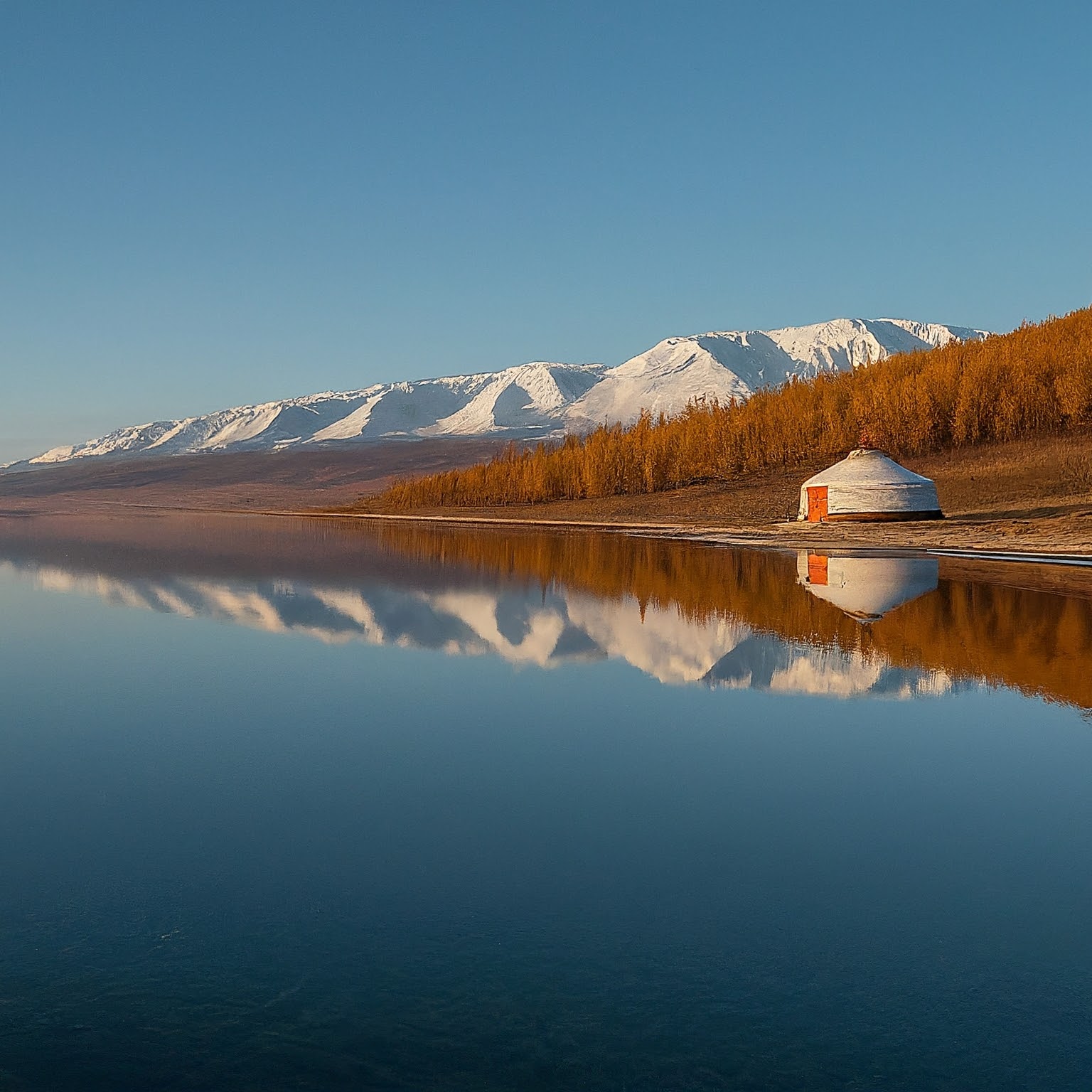 Traditional Mongolian yurt on the shore of Lake Hovsgol, Mongolia, with mountains reflected in the water at sunrise.