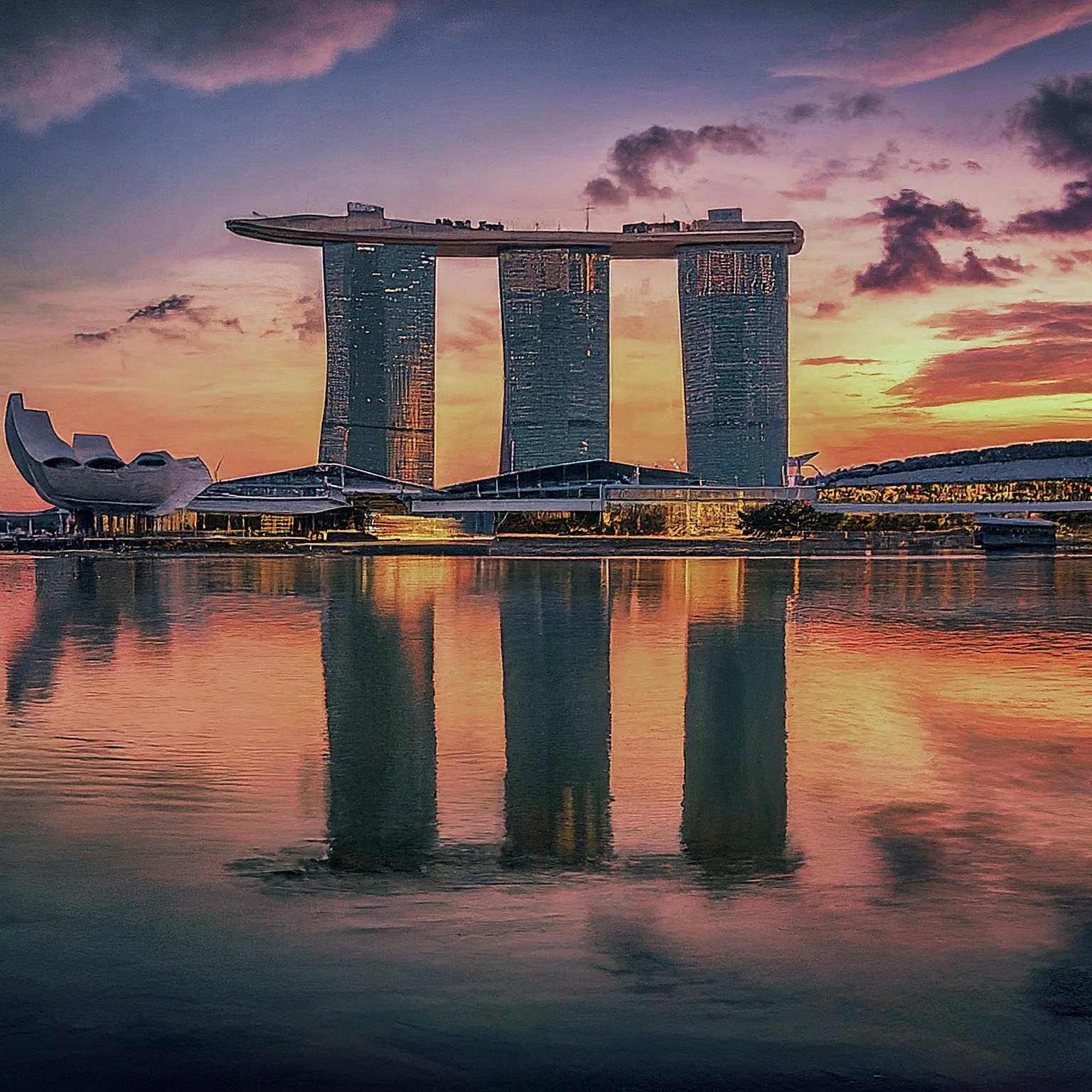 Marina Bay Sands hotel in Singapore at sunset with colorful sky reflections.