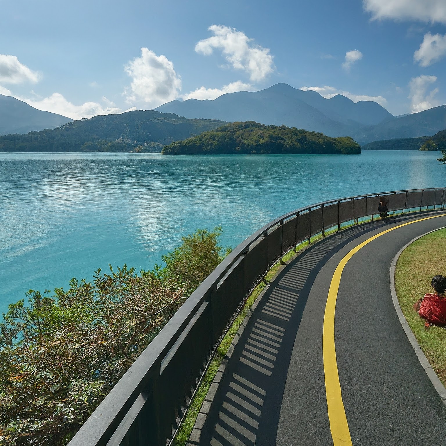 Bicycle path along the shore of Sun Moon Lake, Taiwan, with cyclists and mountain views.
