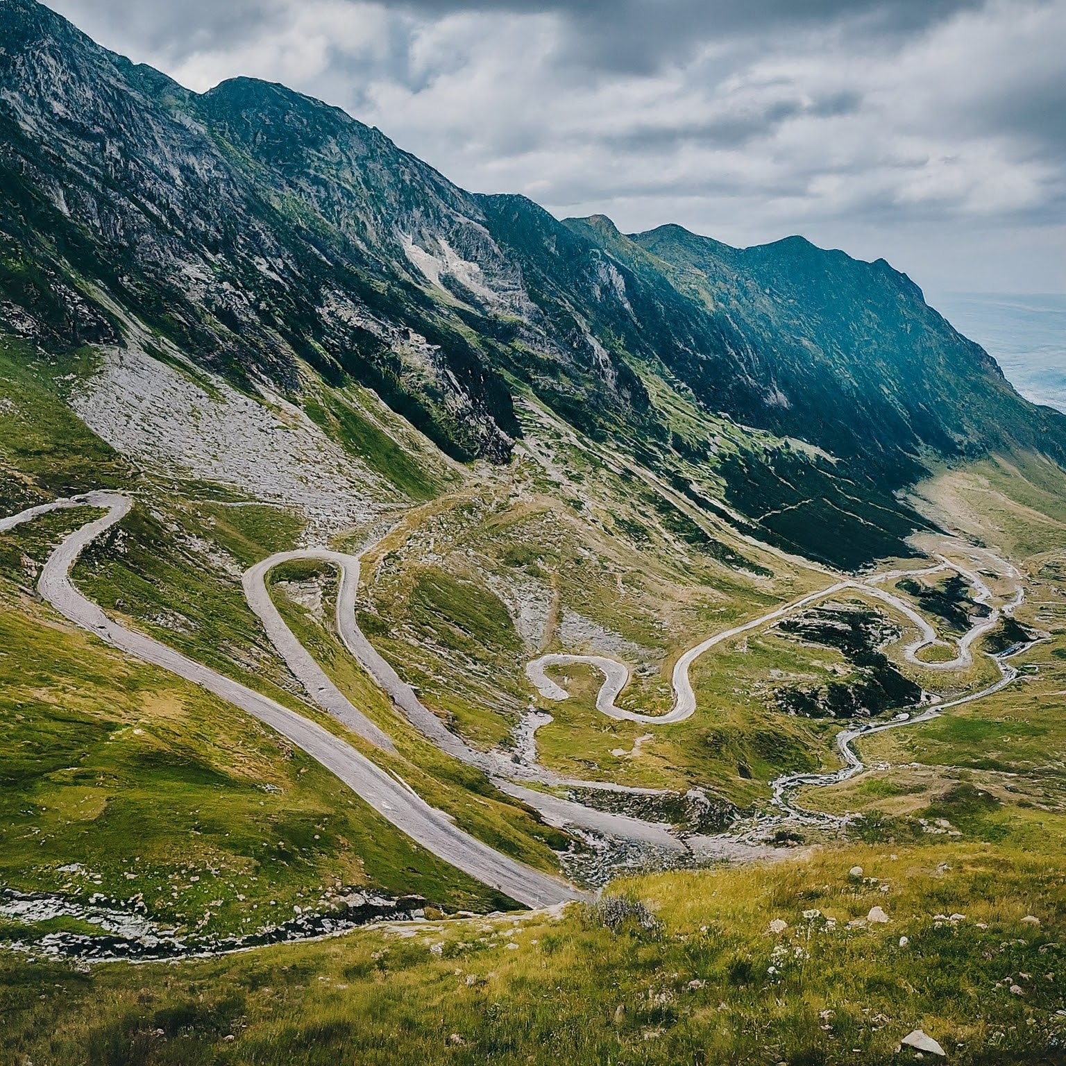 Cyclist on a scenic bend of the Transfagarasan Road in Romania, with mountain views.