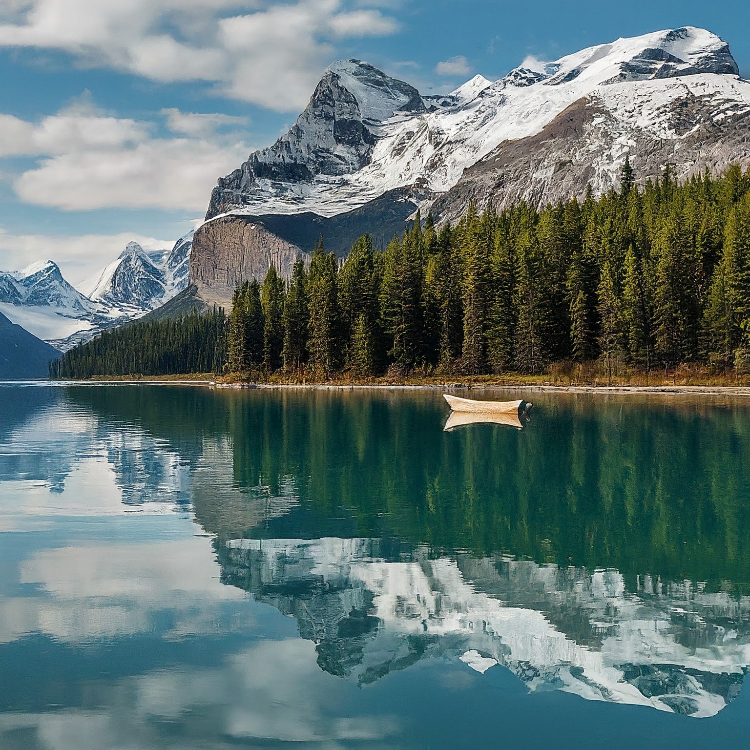 Maligne Lake in Jasper National Parks in Canada, with snow-capped mountains, evergreen forest, and a boat.